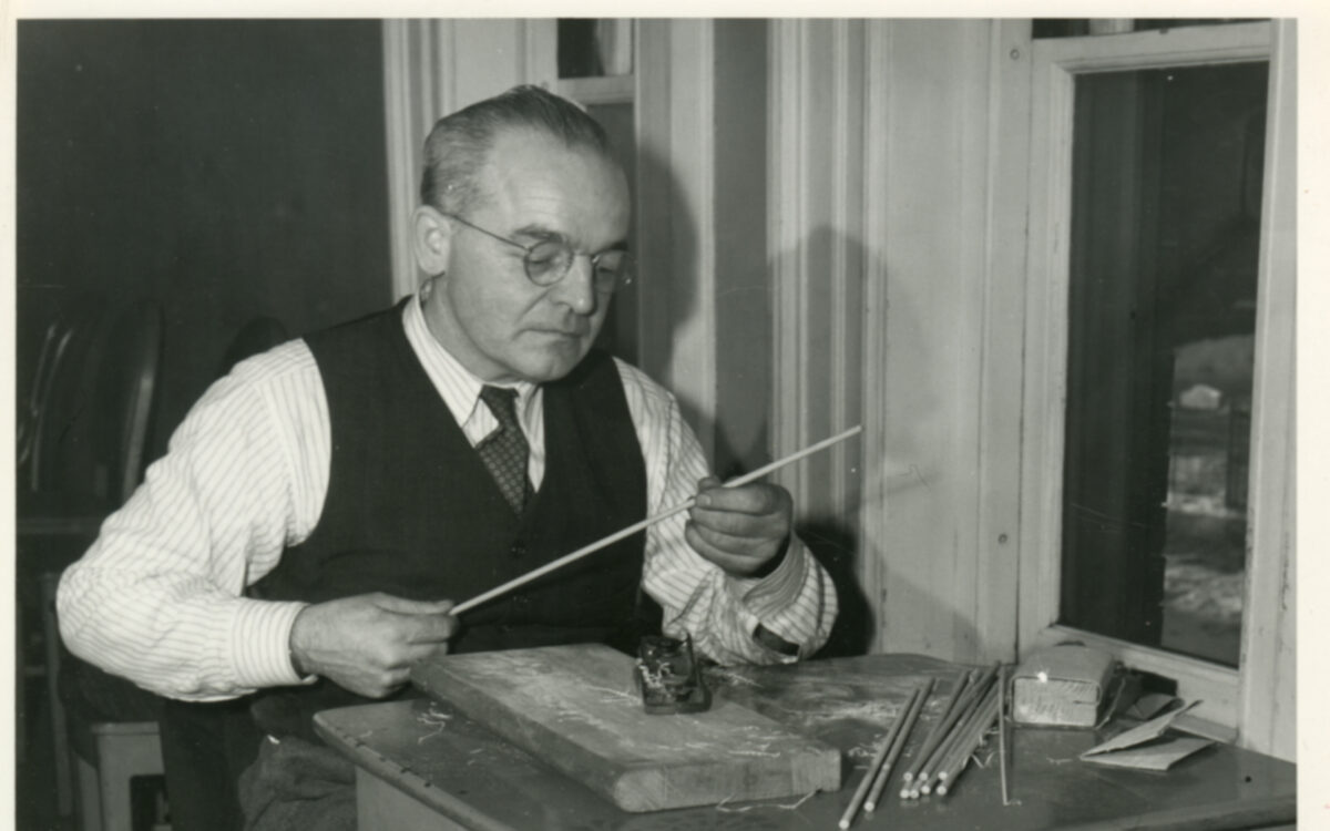 A man sits at a desk holding a wooden towel in process of being made into a baton