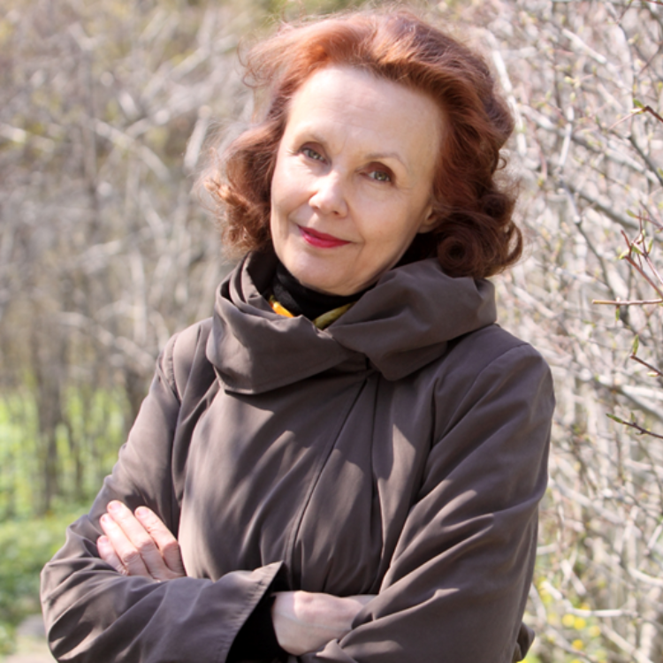 Kaija Saariaho standing outside by some bare trees