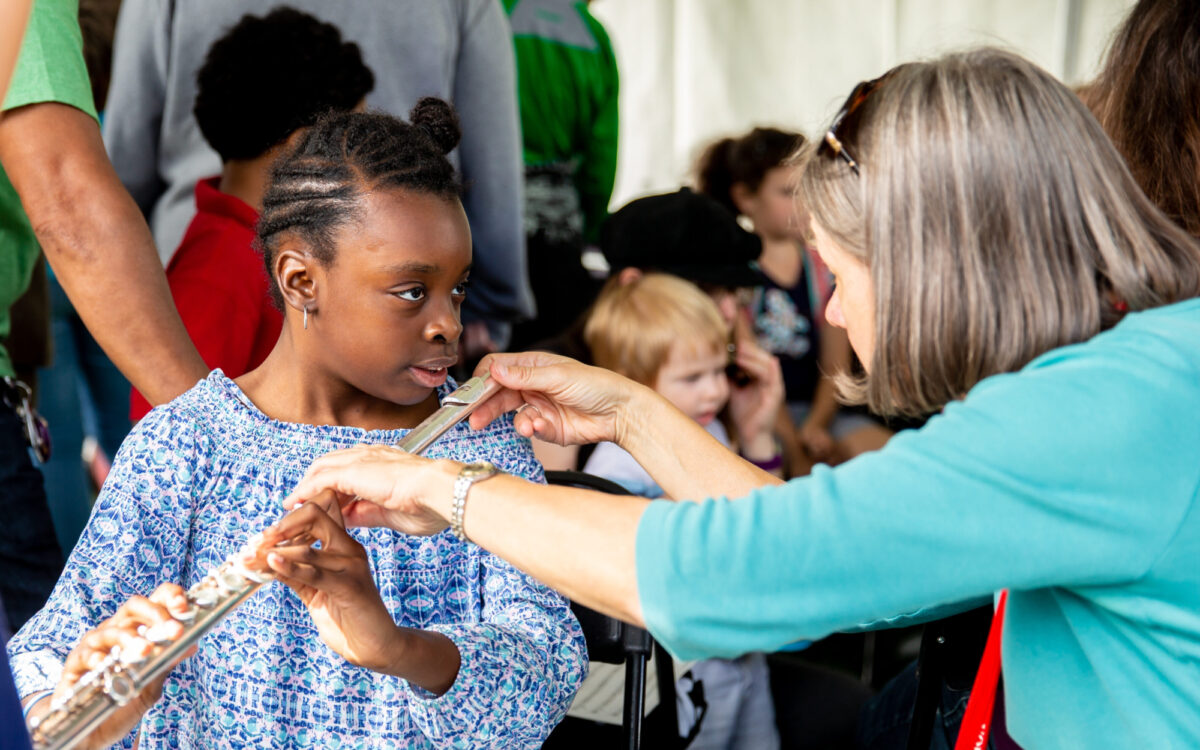 A woman showing a young girl how to play the flute
