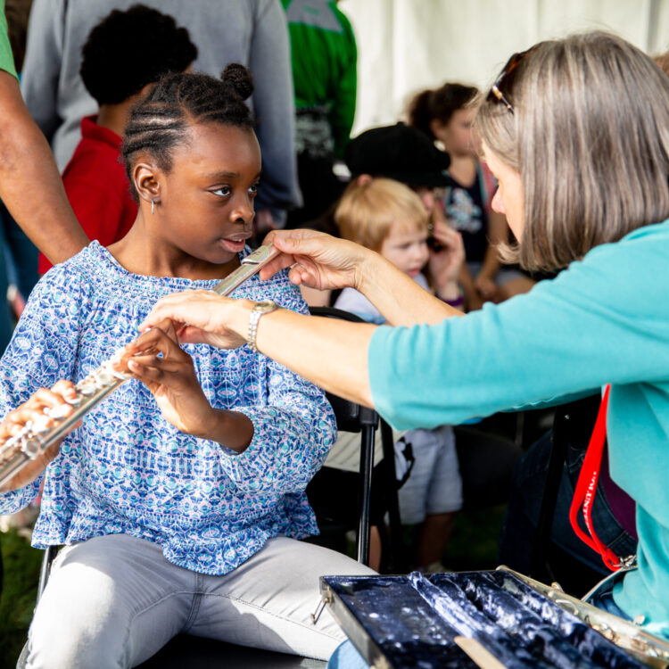 A woman showing a young girl how to play the flute