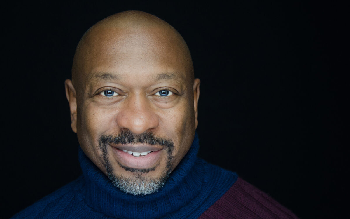 Closeup headshot of smiling man wearing a blue turtleneck sweater