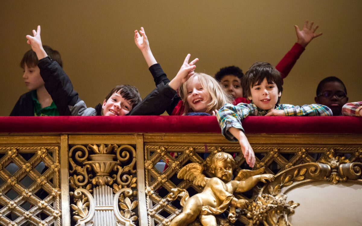 Children standing in a balcony at Symphony Hall posing and throwing their arms up in the air.