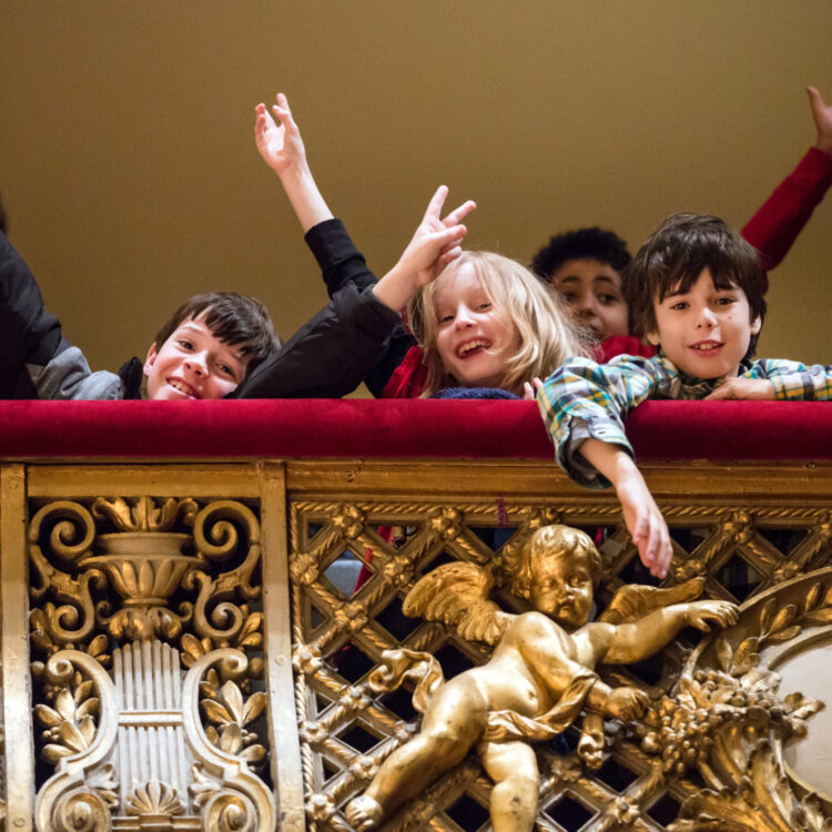 Children standing in a balcony at Symphony Hall posing and throwing their arms up in the air.