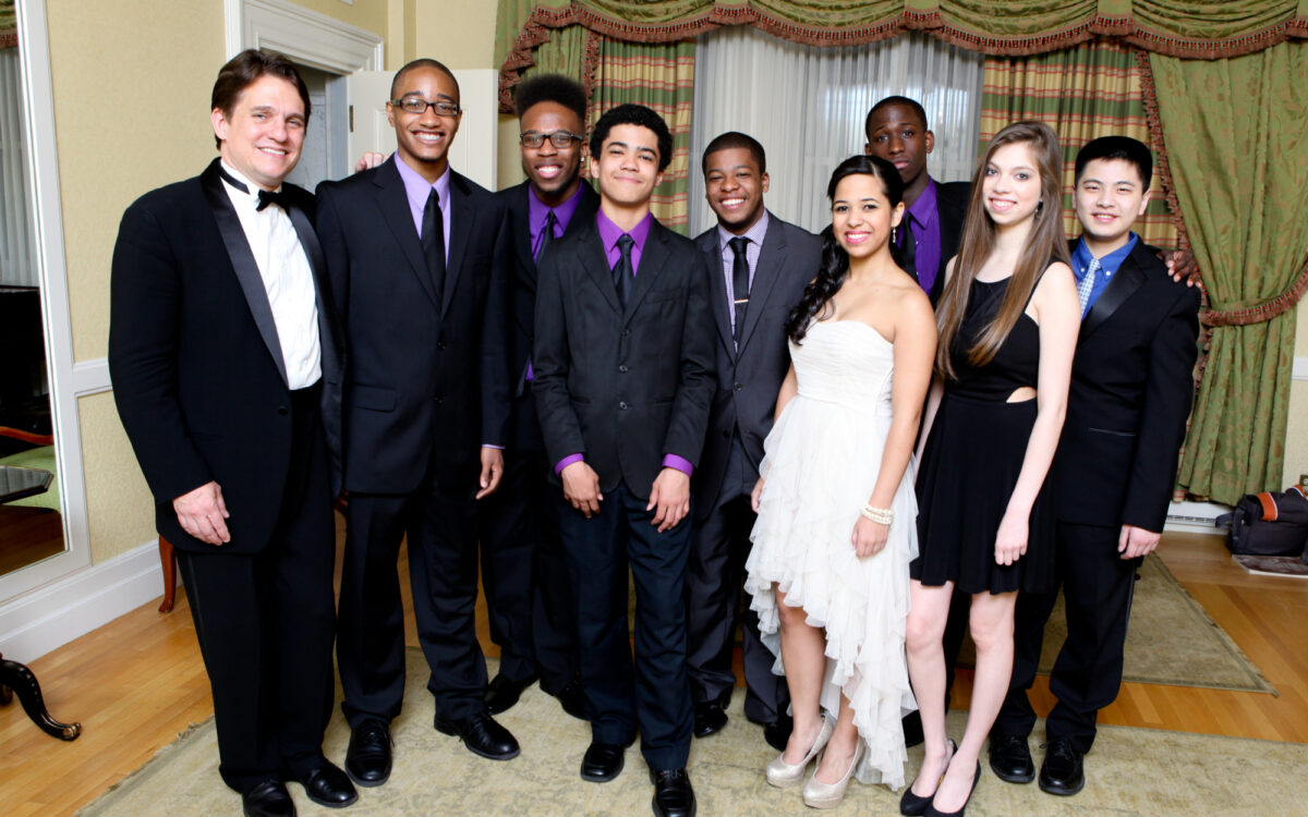 Keith Lockhart stands with eight high school students, all dressed formally before before performing in a Pops concert.