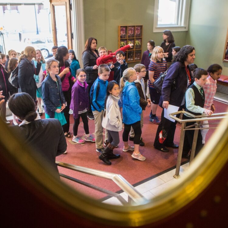 Students and their teacher enter the Symphony Hall lobby. You can see their bus in the background.