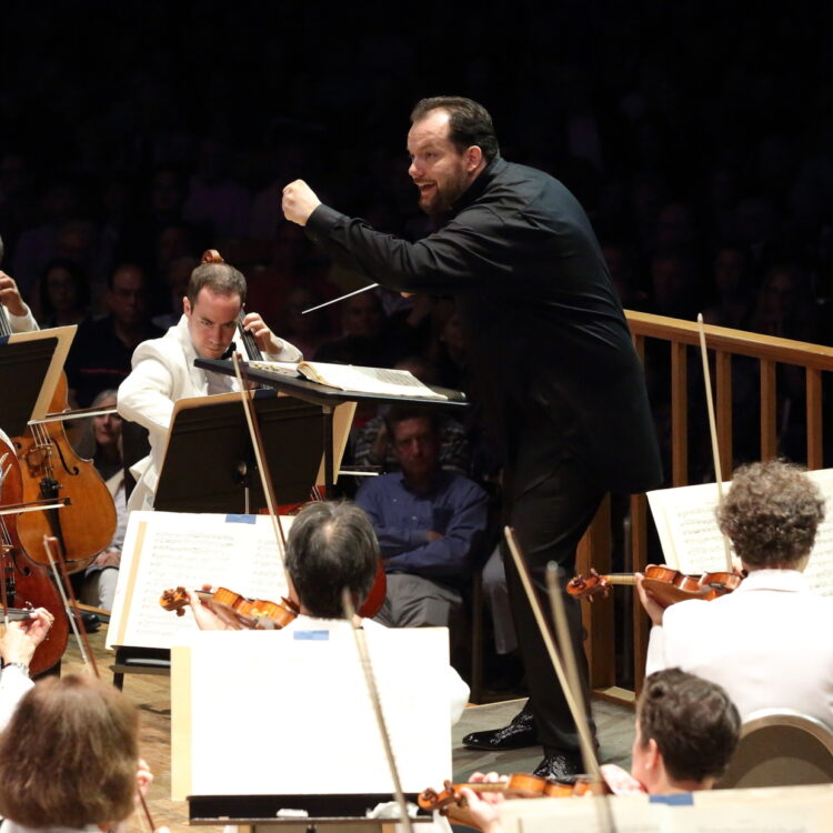 Andris Nelsons is dressed in all black and raises his fist while conducting the BSO in the Koussevitzky Music Shed