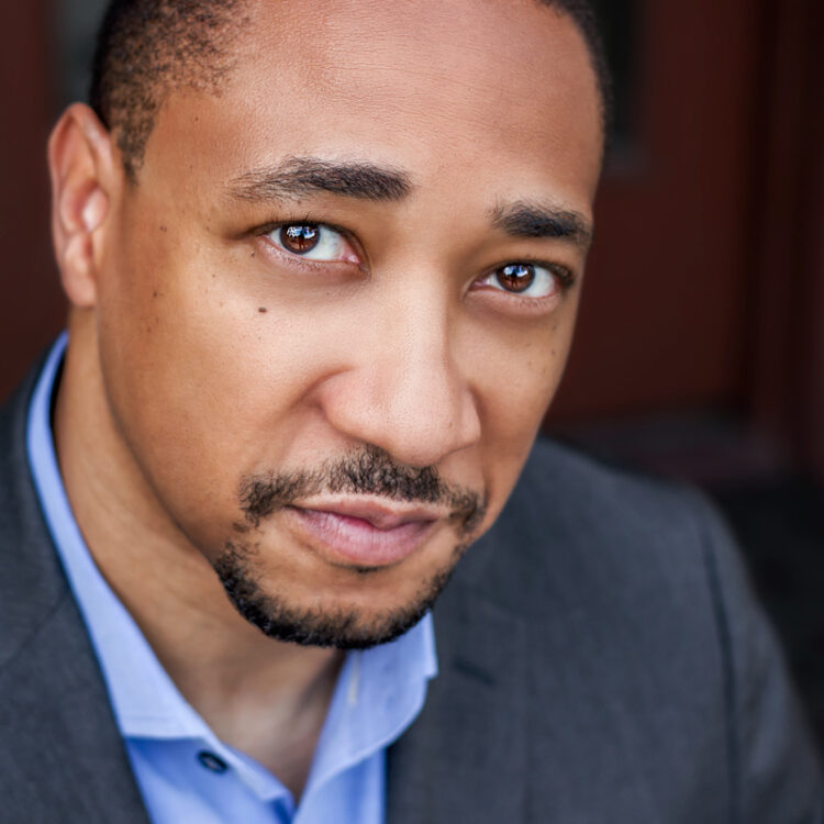 Headshot of Damon Gupton wearing a grey suit and a blue collared shirt