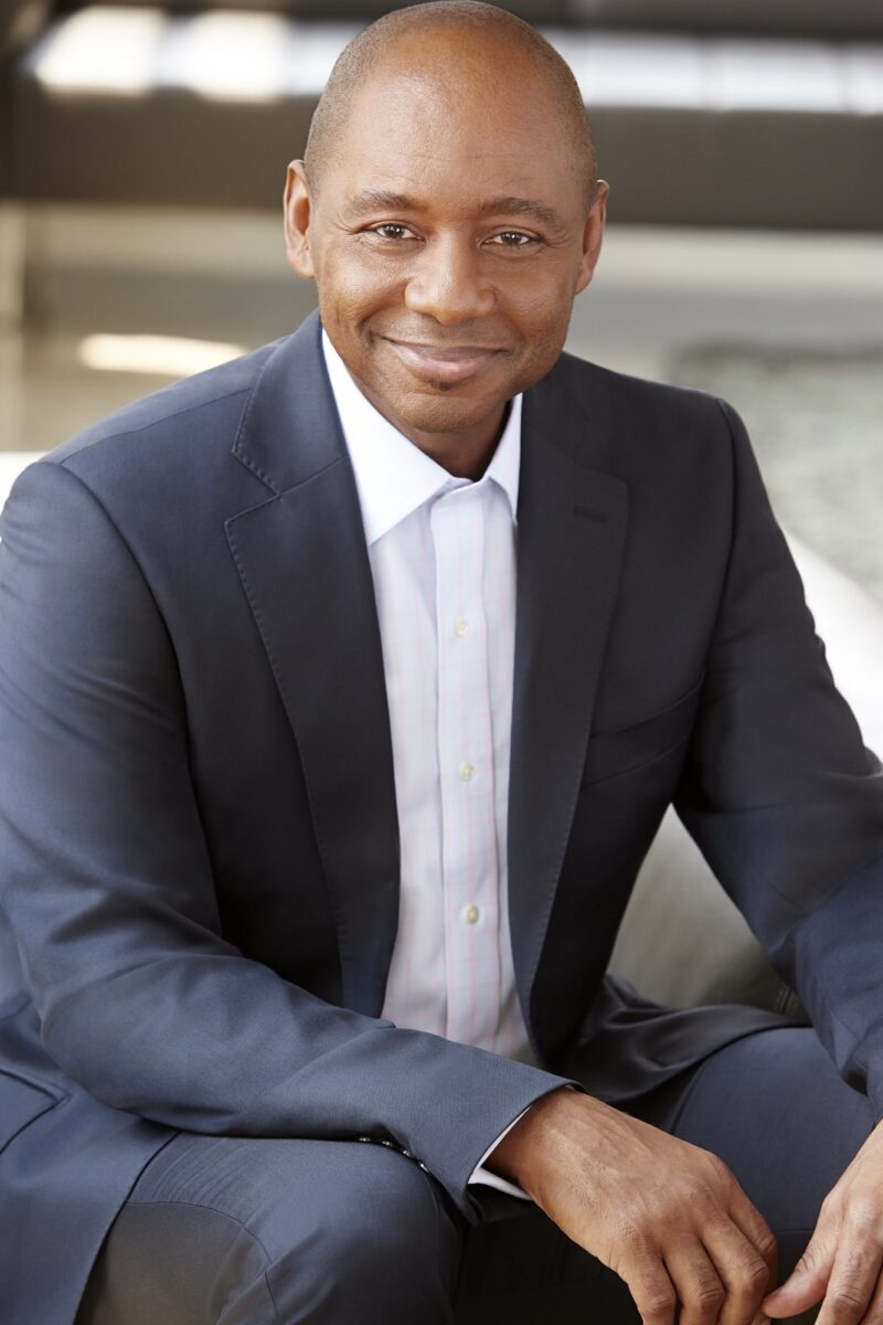 Brandford Marsalis wearing a navy suit and white collared shirt sitting down