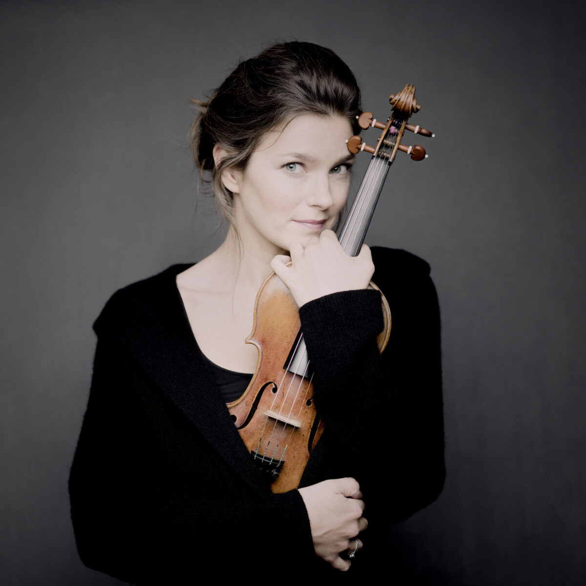 Janine Jansen holding her violin in front of a grey background