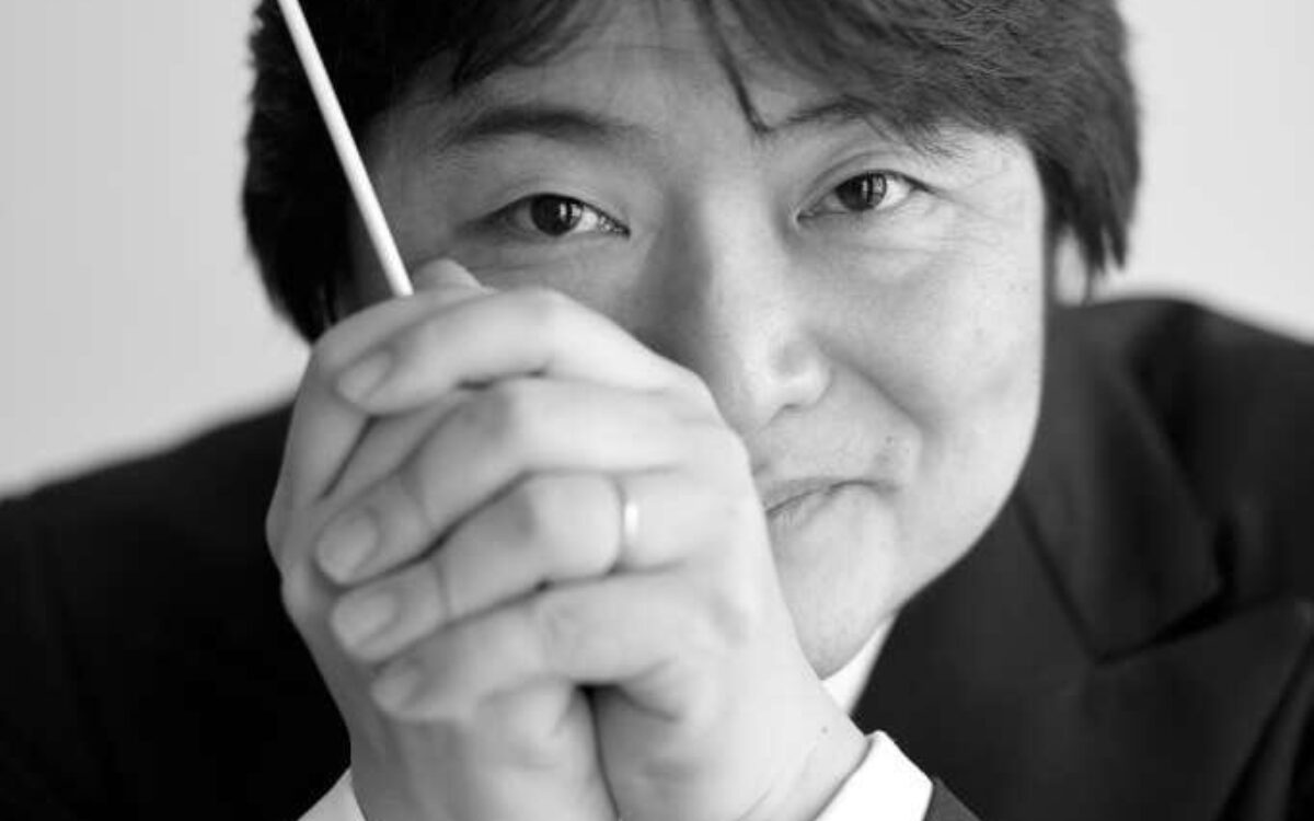 Kazuki Yamada holding a conductor's baton in front of his face, smiling