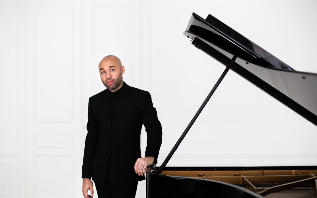 Aaron Diehl dressed in black standing next to a piano with its lid open.