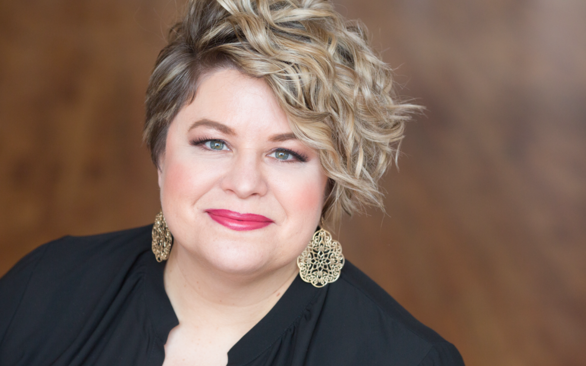 Amber Wagner headshot wearing decorative gold earrings and a black top