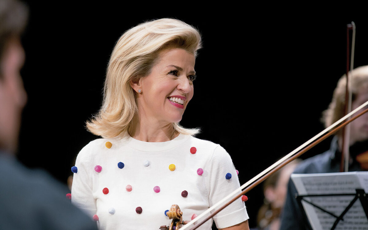 portrait of Ann Sophie Mutter holding her violin while wearing a white top with multicolored plush dots