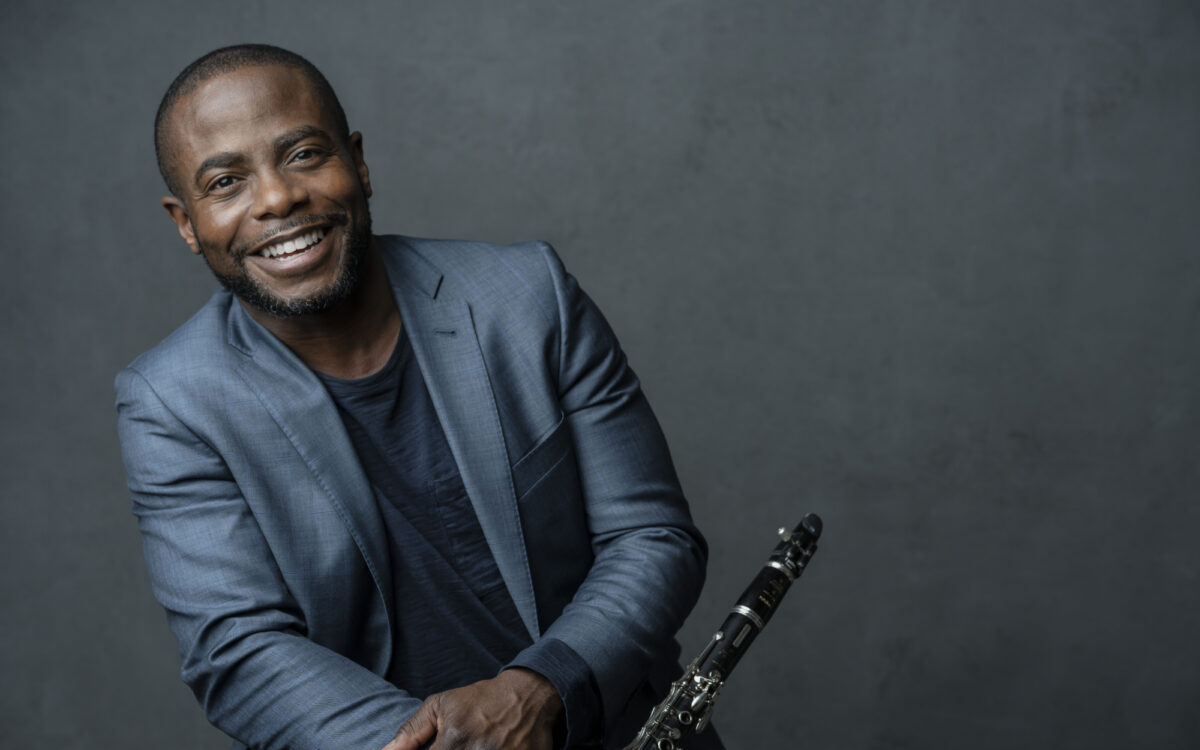 Anthony McGill holding a clarinet and smiling in front of a gray background