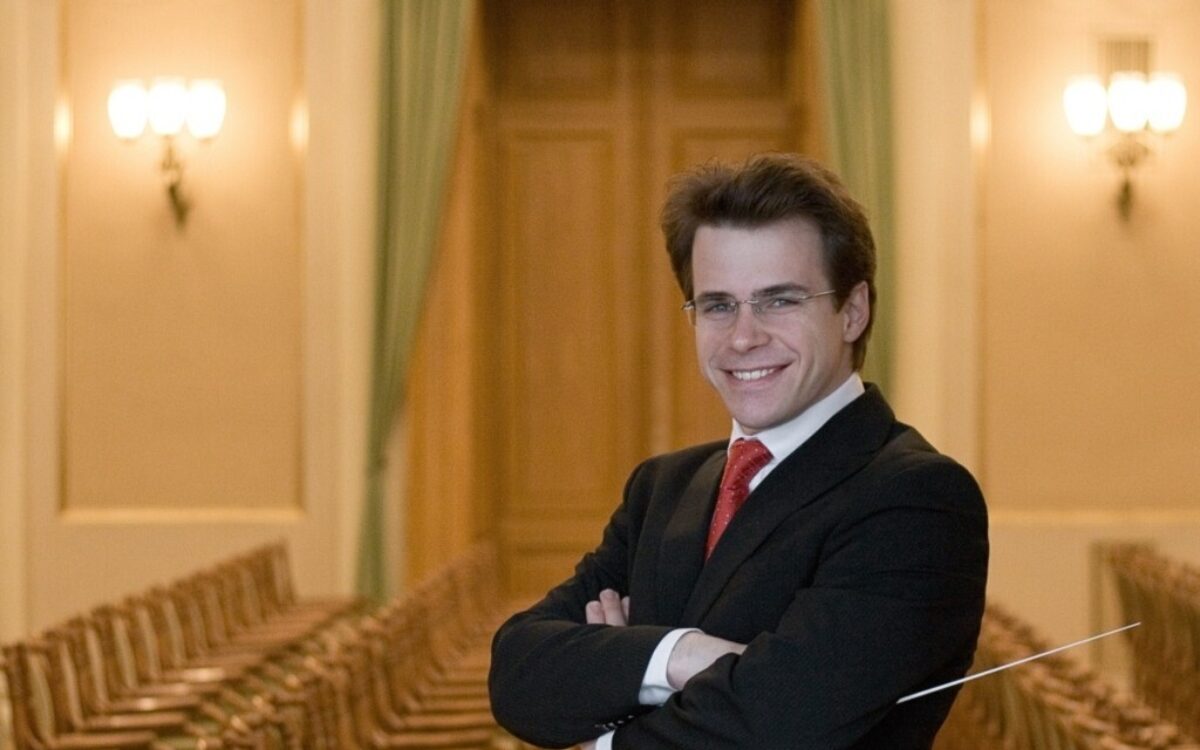 Jakub Hrůša, conductor with his arms crossed, holding a baton and smiling