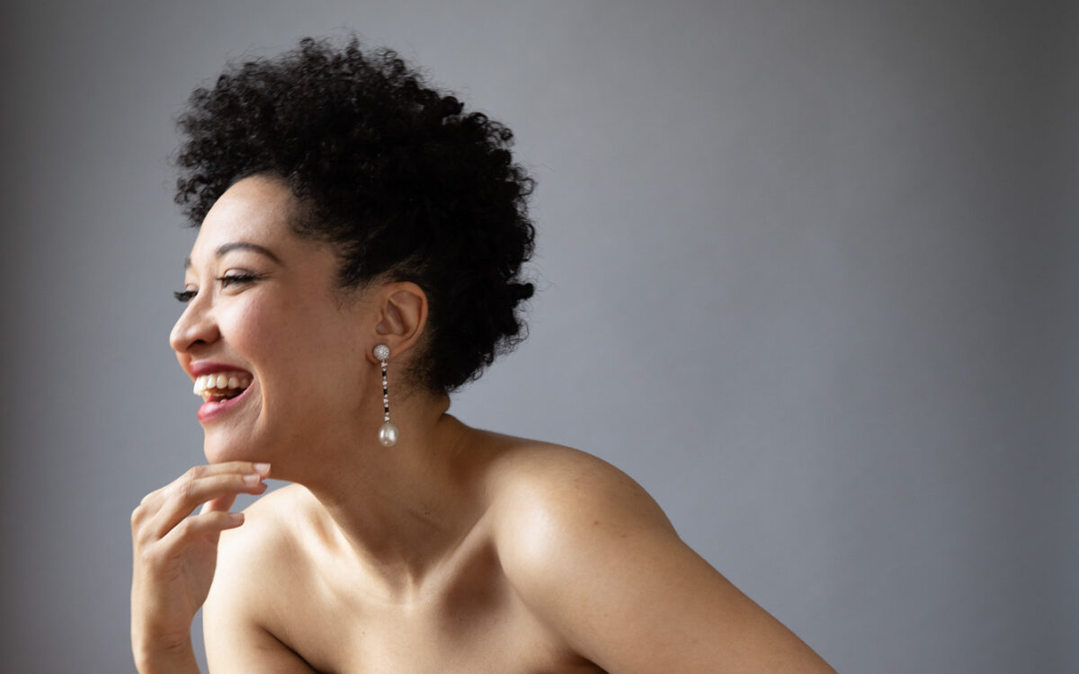 Julia Bullock wearing a black dress, facing our left, laughing