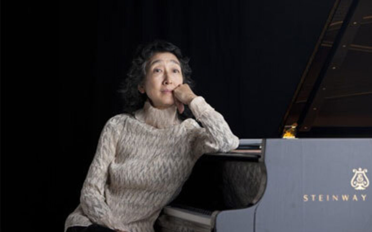 Mitsuko Uchida sitting next to a Steinway piano with her head resting on her hand