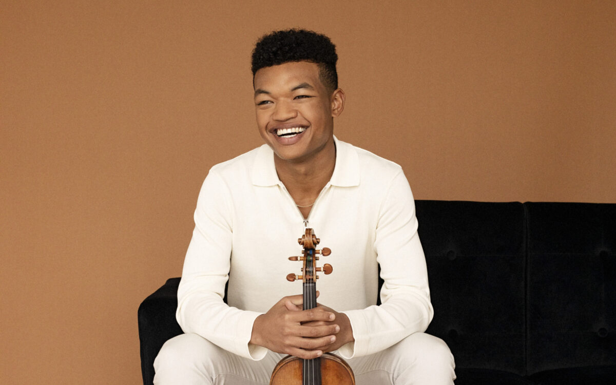 Randall Goosby sitting on a couch holding a violin in front of him