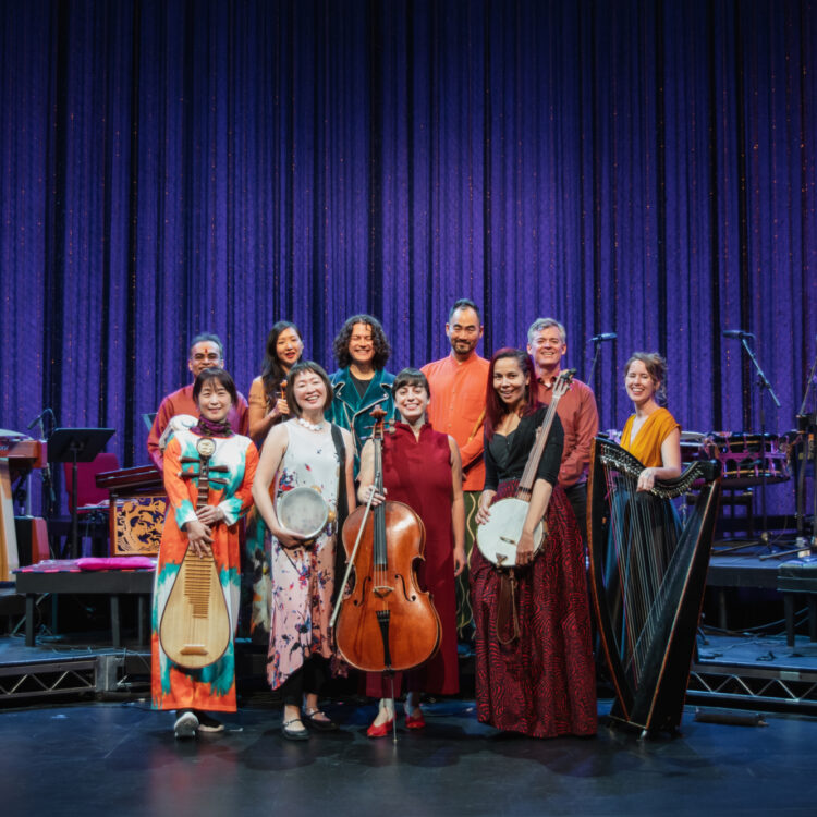 Ten musicians posing onstage with their instruments, dressed in colorful outfits