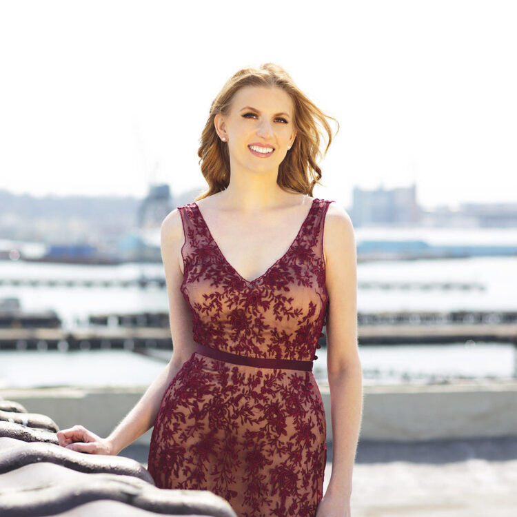 Photo of Amanda Majeski wearing a maroon gown standing outside in front of a body of water