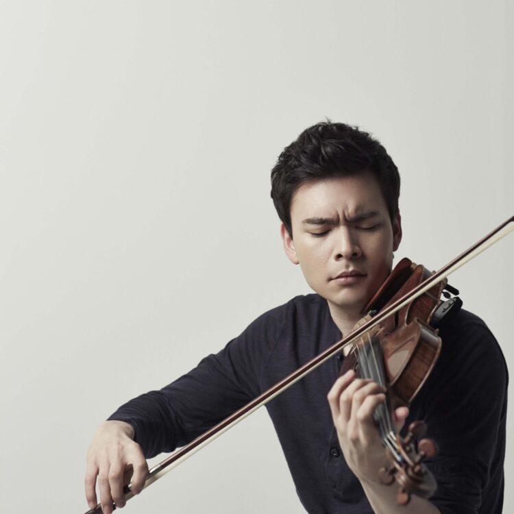 Stefan Jackiw playing a violin against a beige background