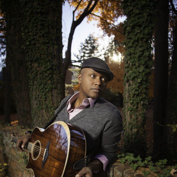 Javier Colon holding a guitar and looking to his left over his shoulder