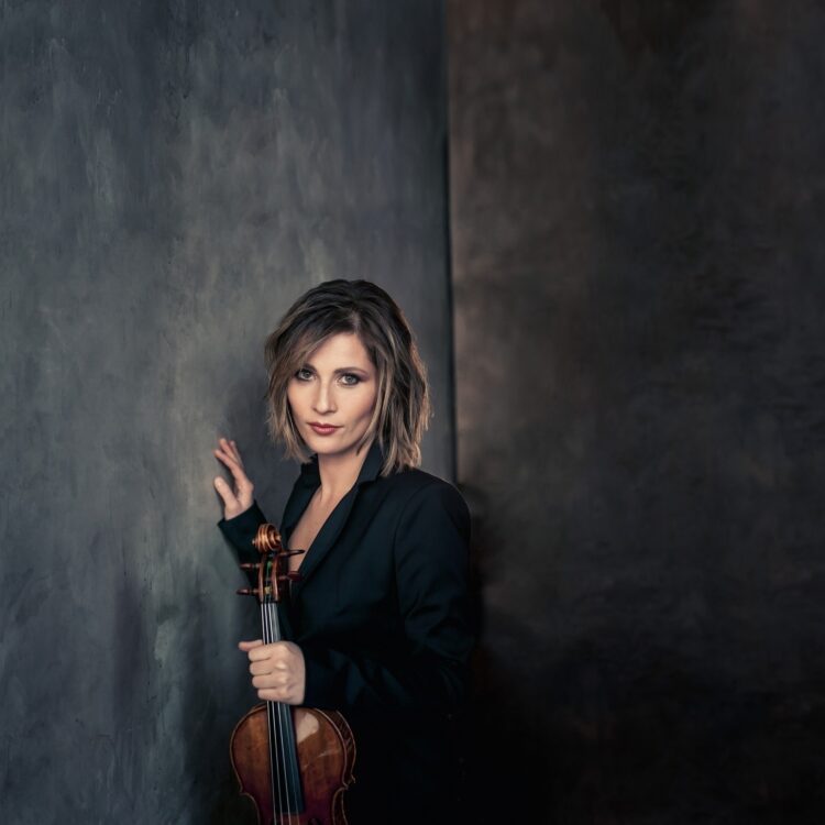 Lisa Batiashvili standing by a wall, holding her violin in front of her