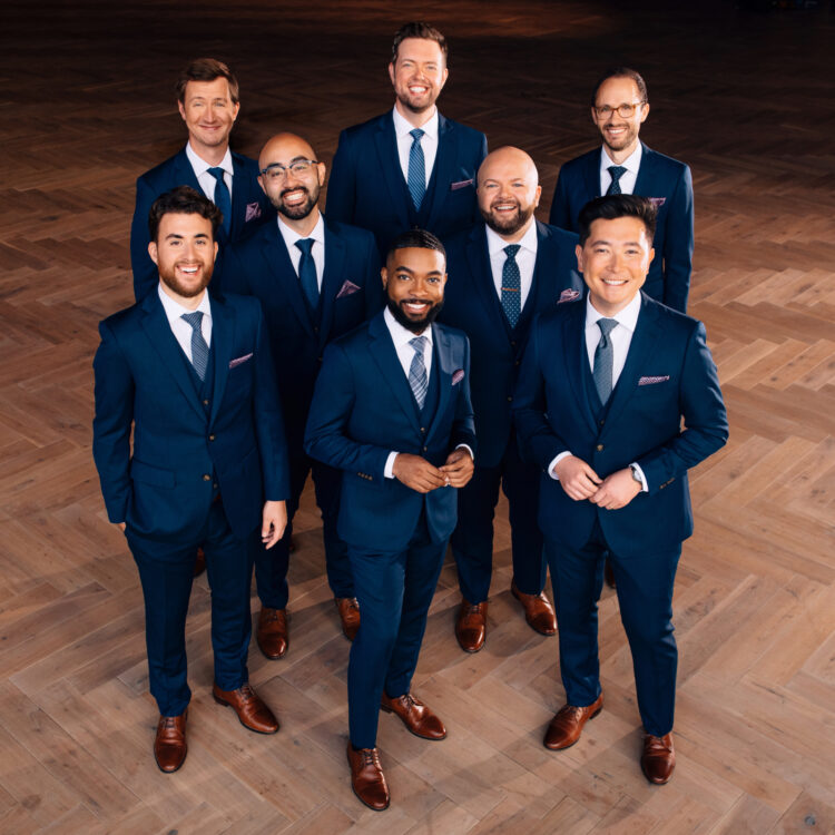 Eight singers dressed in navy suites and posing for the camera