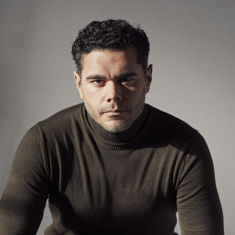 Elliot Madore sitting on a block of wood wearing a turtleneck