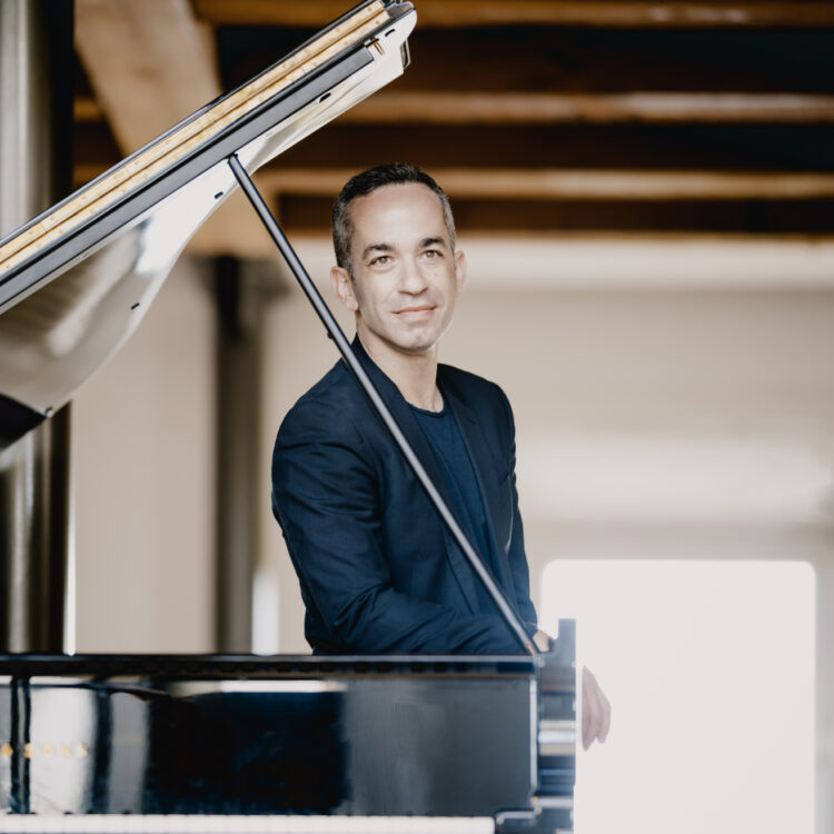 Inon Barnatan standing behind a piano