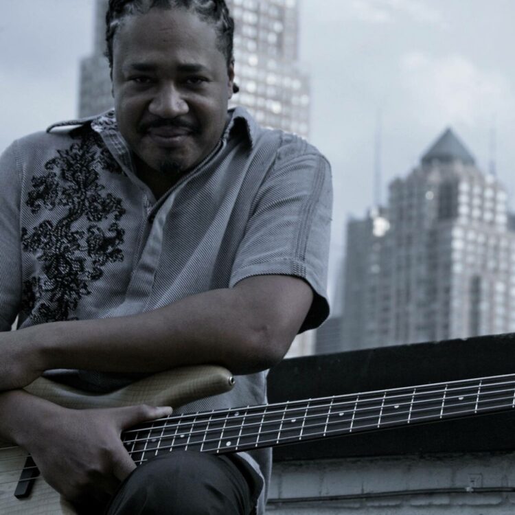 James Genus sitting outside with his bass guitar on his lap