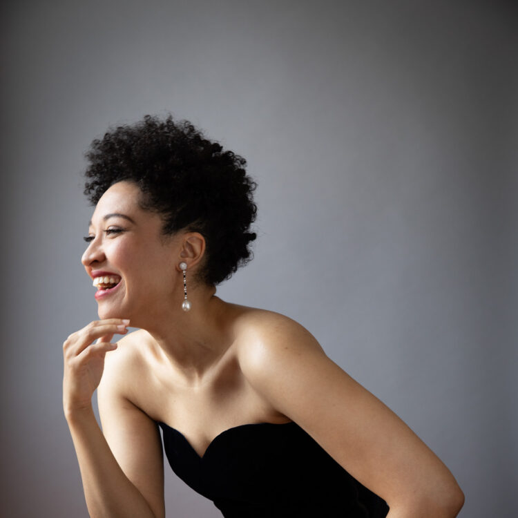 Julia Bullock wearing a black dress, facing our left, laughing