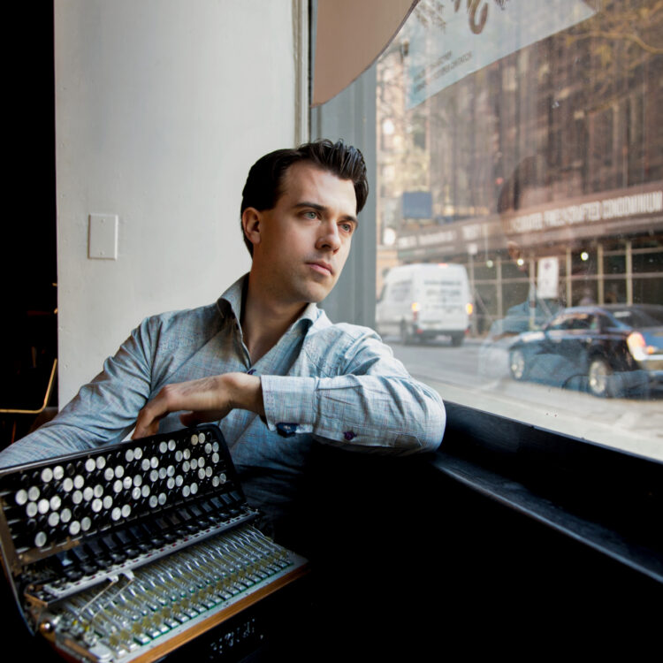 Photo of Julien Labro sitting down with his accordian looking out a window.