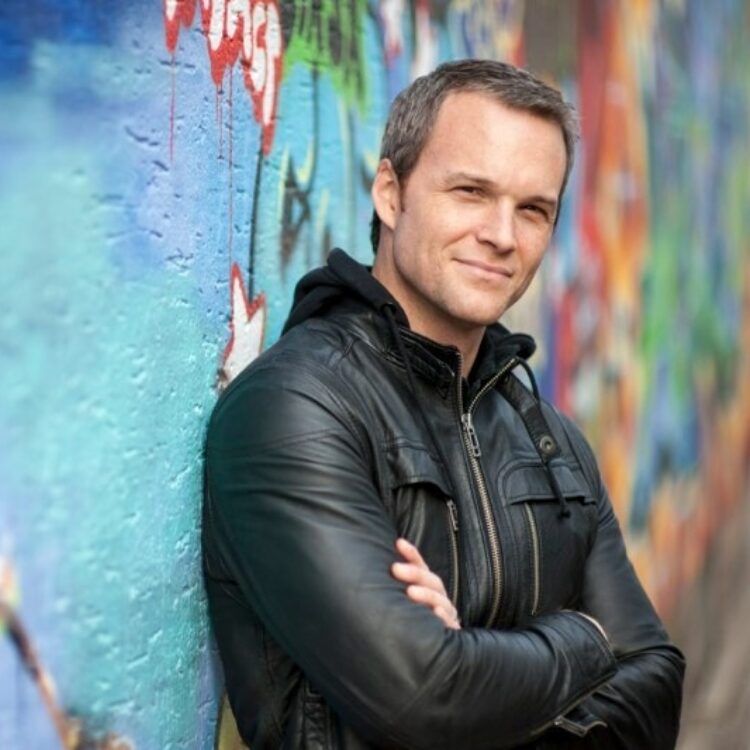 Headshot of Ryan McKinny standing with his arms crossed and leaning against a colorful wall