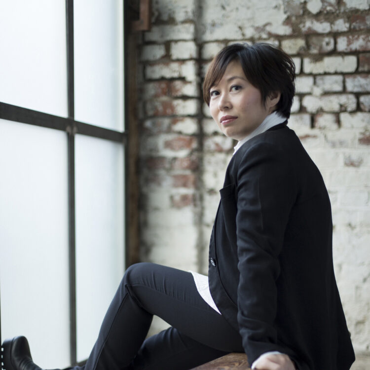 Xian Zhang sitting on a bench in front of a window