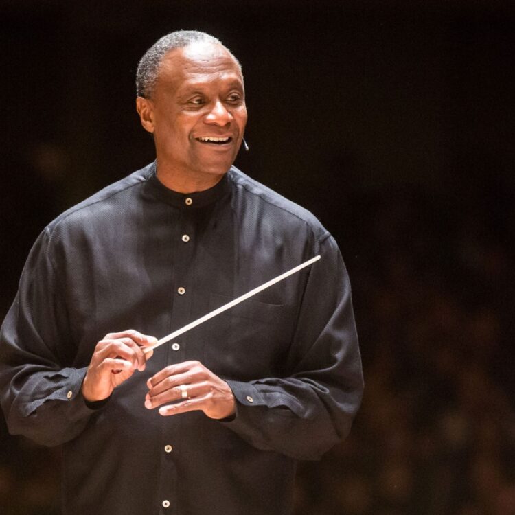 Conductor Thomas Wilkins holding his baton and smiling onstage.