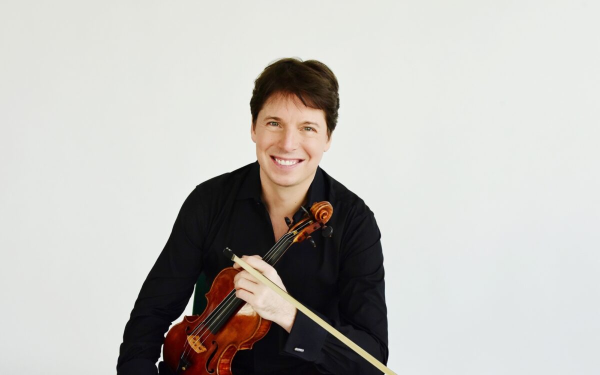 Joshua Bell sitting on a stool, holding his violin and smiling