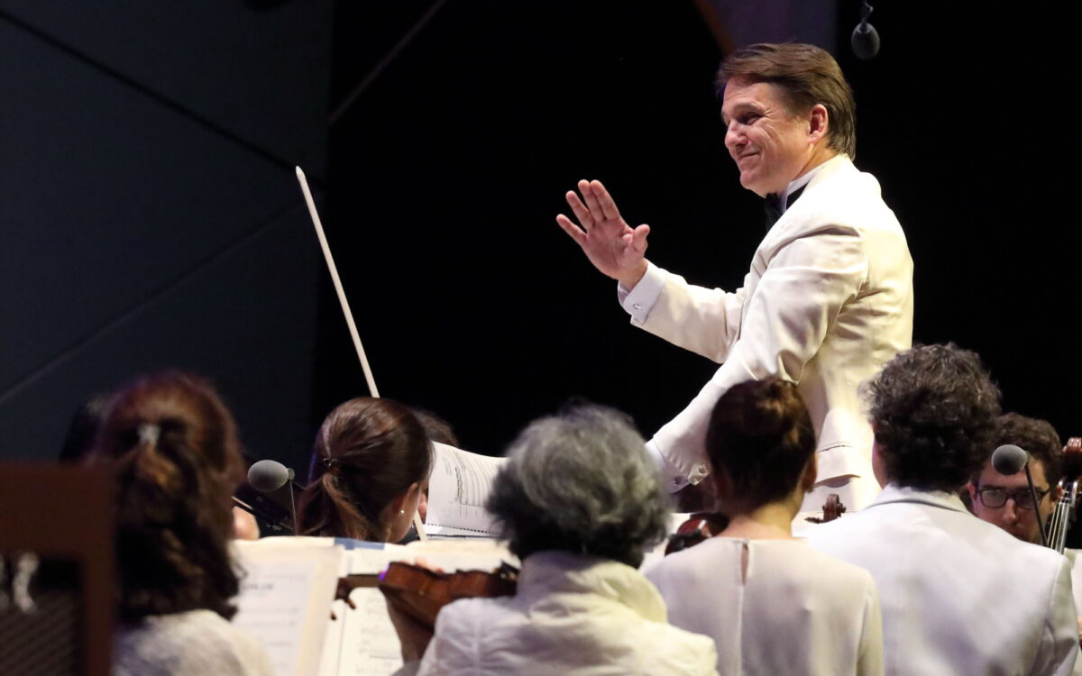 Keith Lockhart wears a white suit jacket and smiles while conducting the Boston Pops