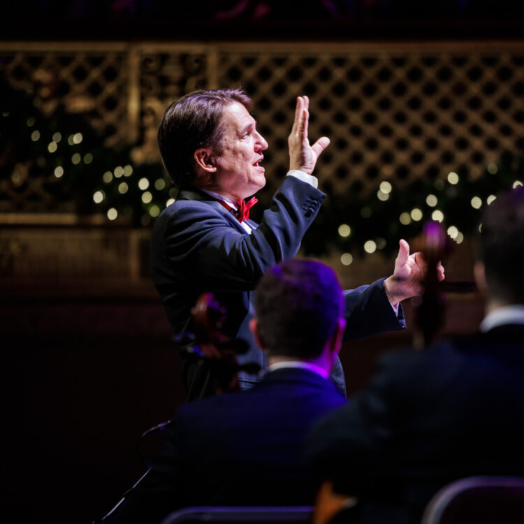 A close-up view of Keith Lockhart conducting the Boston Pops and wearing a black tuxedo with a red bowtie