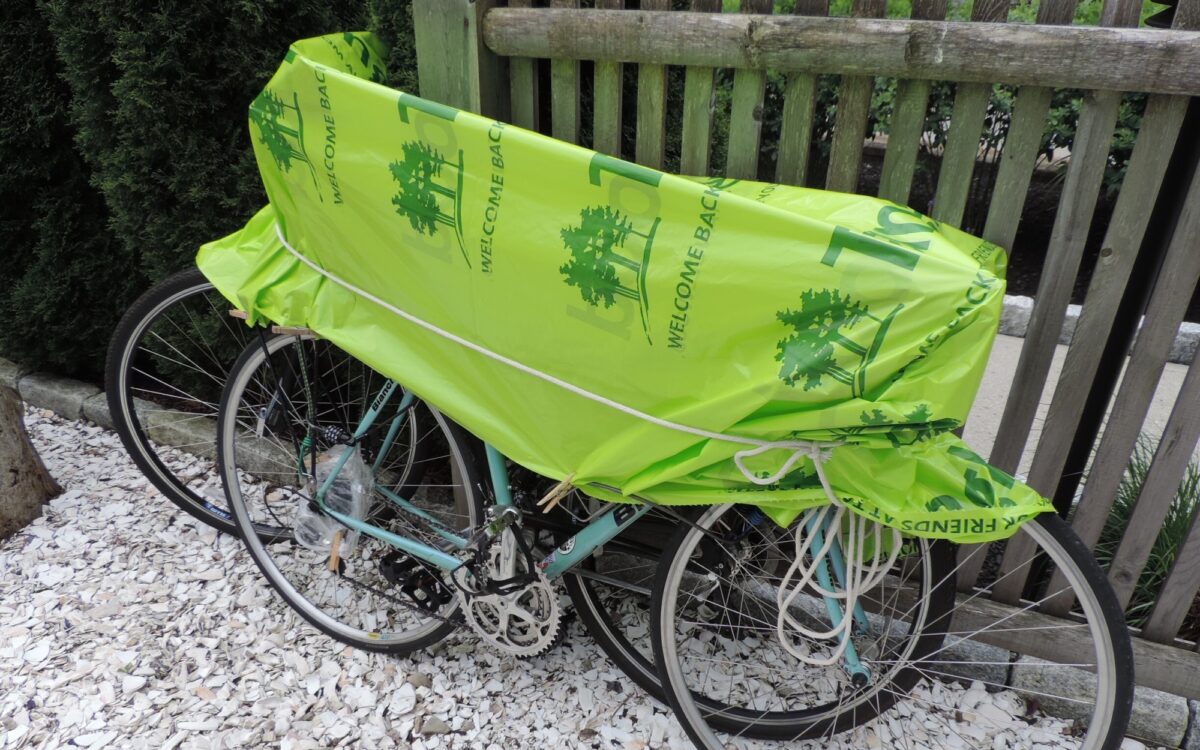 A green tarp covers two bicycles parked against a railing outside