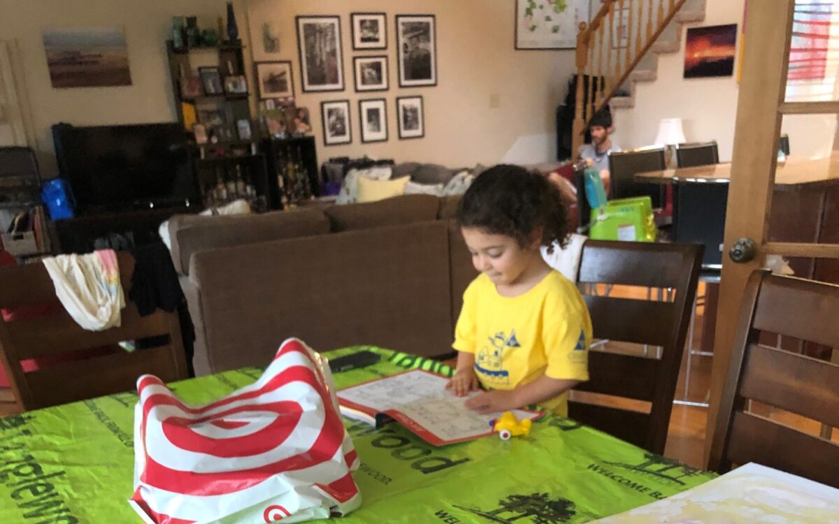 A little girl reads a book by three finger paintings sitting on a green tarp