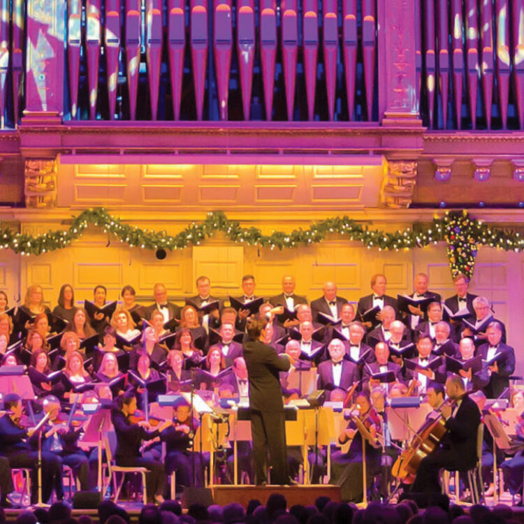 The Boston Pops and Tanglewood Festival Chorus perform on the Symphony Hall stage, which is lit with a bright purple light and projections of snowflakes