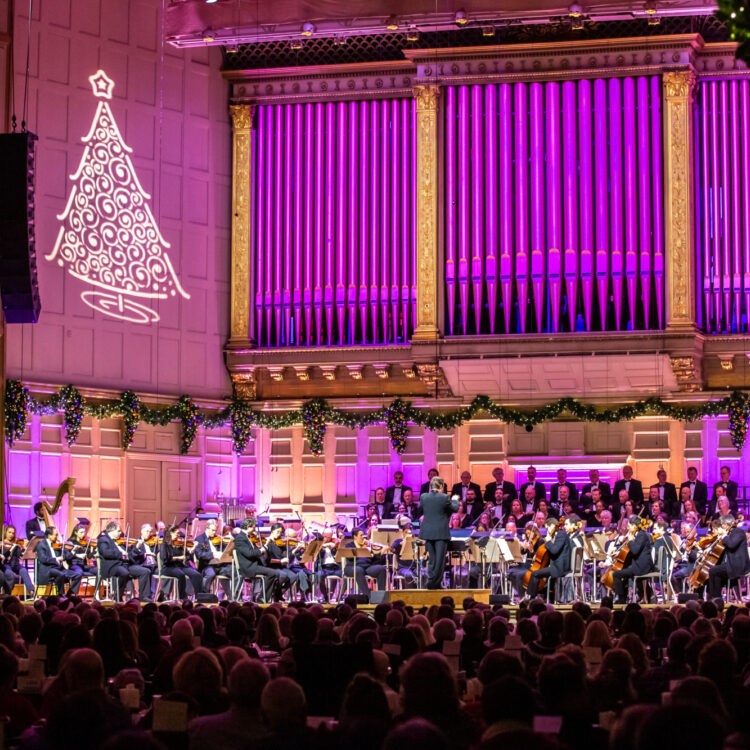 Boston Pops and the Tanglewood Festival Chorus performing at Symphony Hall, Boston, with Keith Lockhart conducting. A projection of a Christmas tree is on the wall behind them.