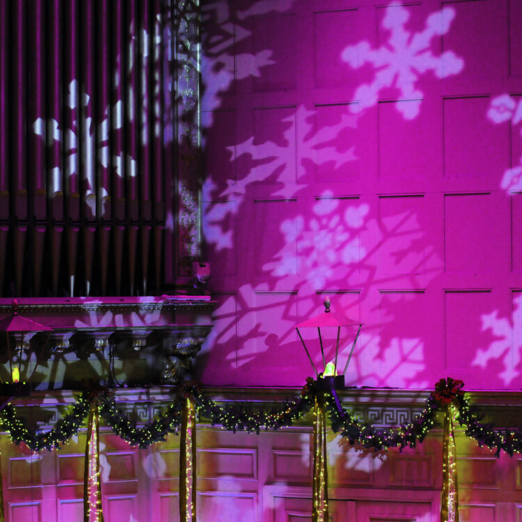 Purple light and white snowflakes are projected on to the wall and organ in Symphony Hall in Boston.