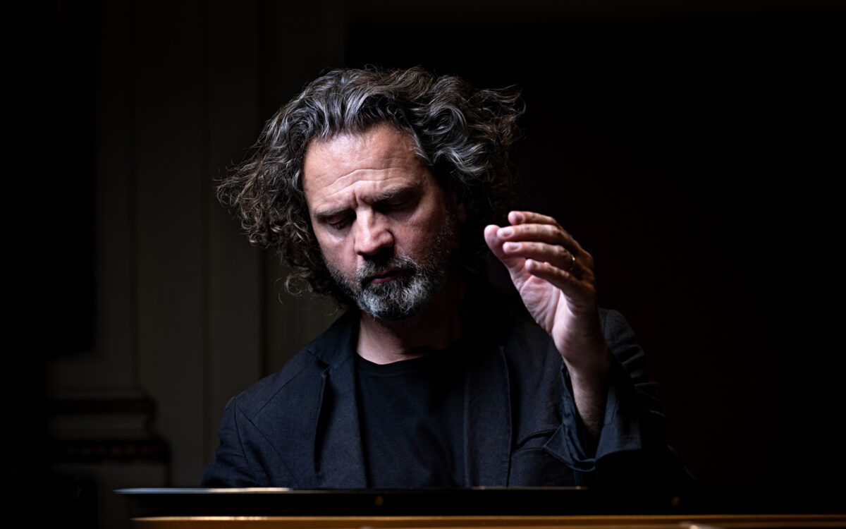 Andreas Haefliger sitting in front of a piano with one hand raised