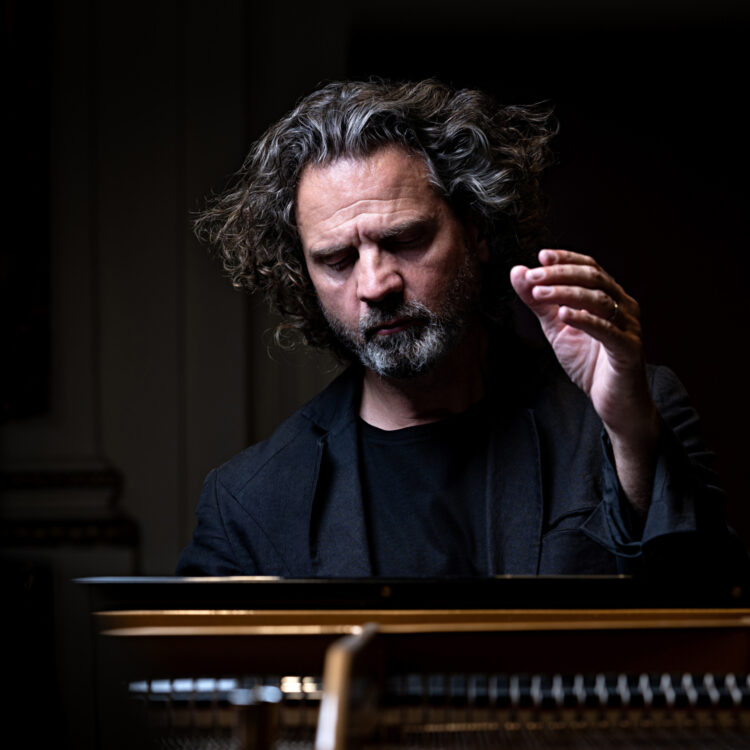 Andreas Haefliger sitting in front of a piano with one hand raised