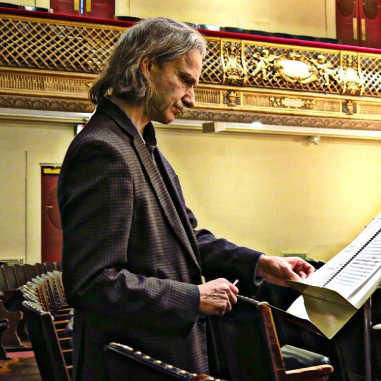 Michael Gandolfi standing in the audience of Symphony Hall looking at a music score on a music stand.