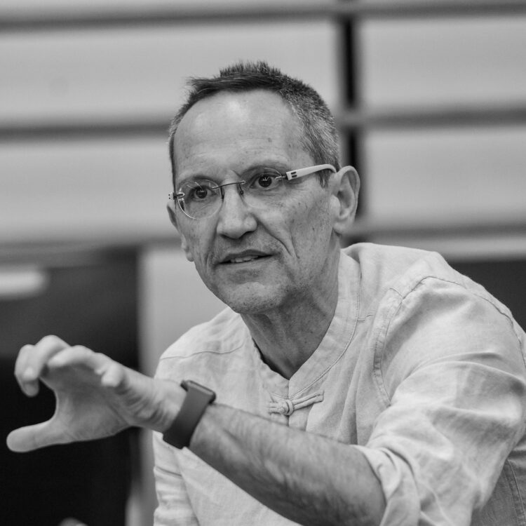 Black and white photo of Osvaldo Golijov sitting in front of a music stand.