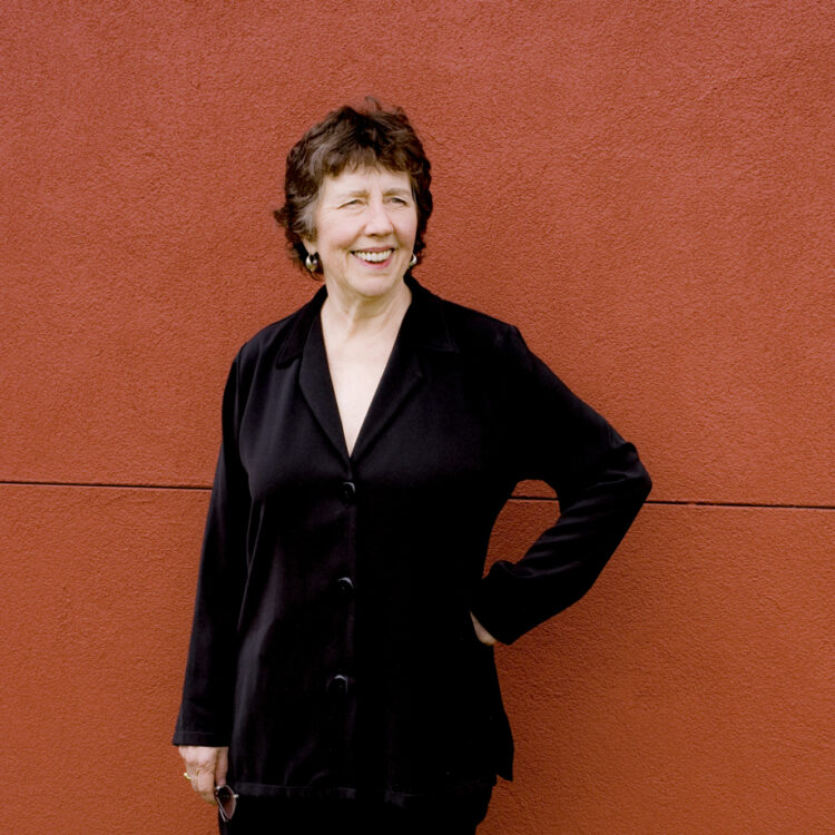 Joan Tower posing in front of a rust-colored building