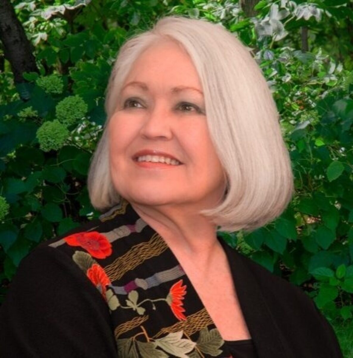 Margo Garrett, wearing a black shirt with a colorlful scarf draped over her left shoulder, looking to her left and smiling